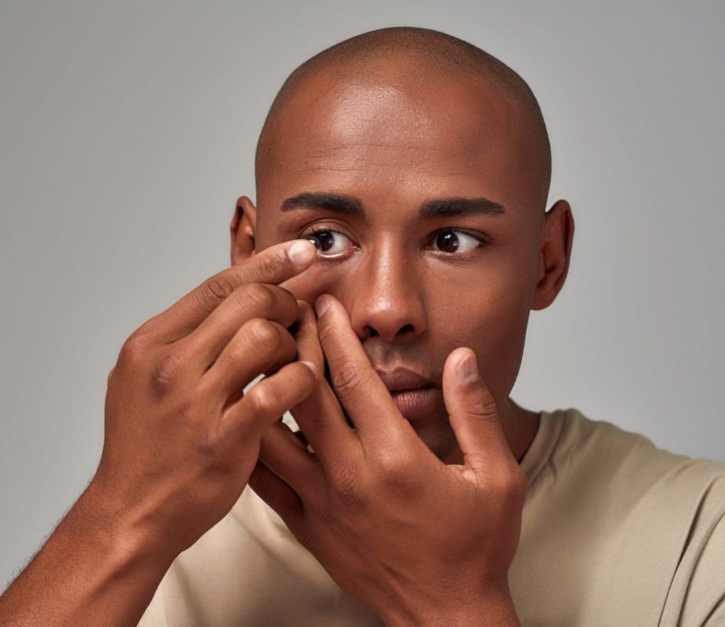 A young man applying a contact lens to his right eye.