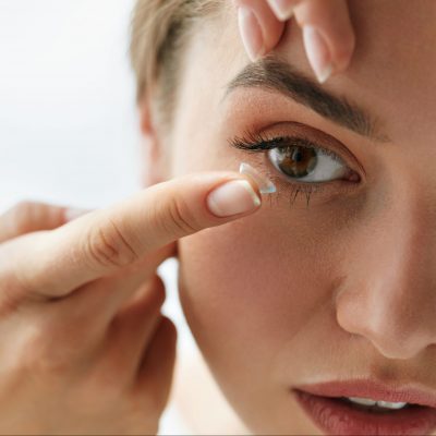 A young woman with a contact lens on her finger tip, preparing to apply it to her eye.